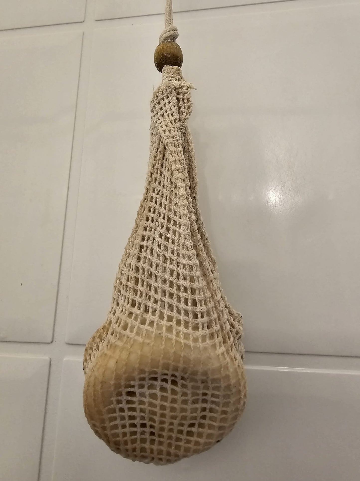 Textured beige bag with a wooden handle hanging against a tiled wall.
