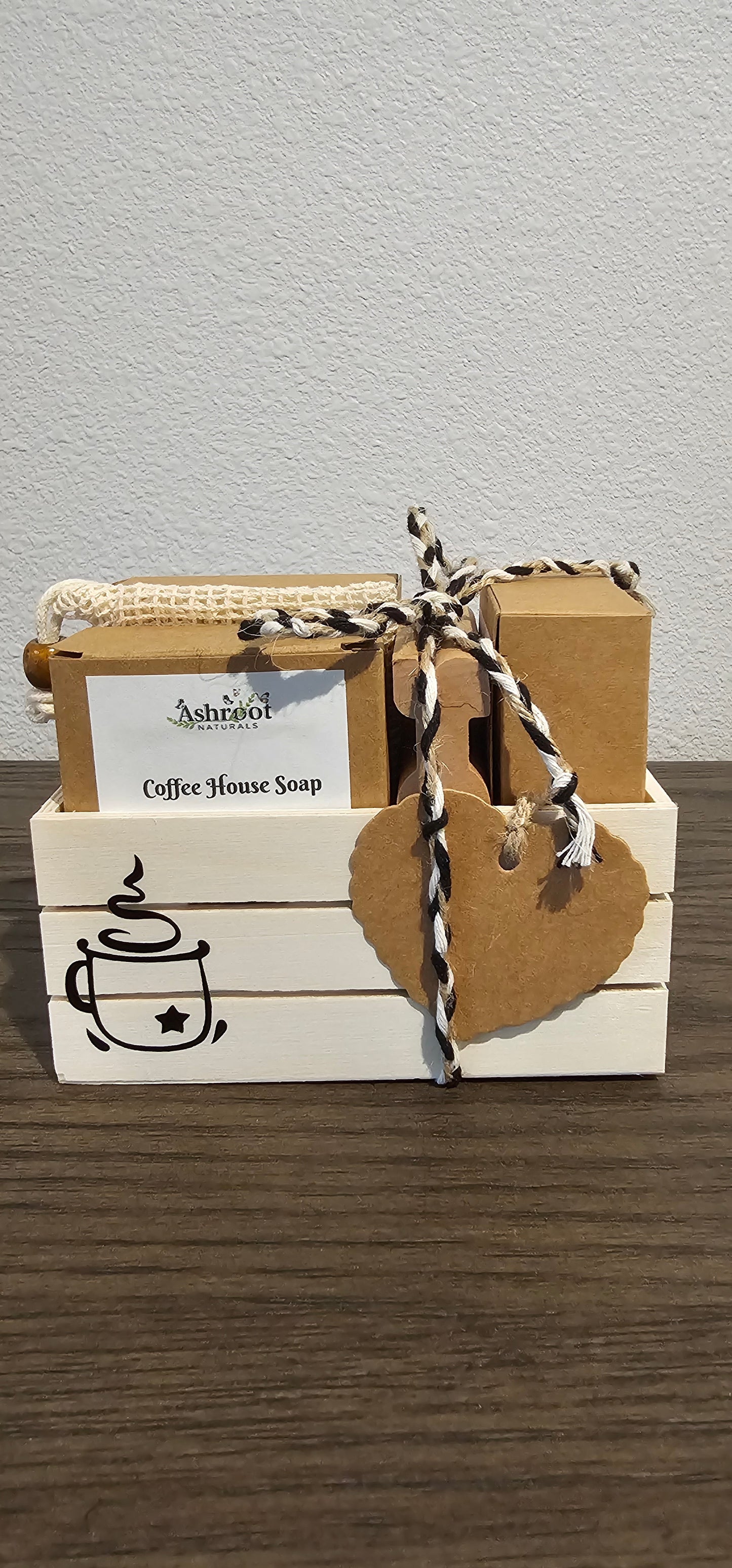 A small wooden crate box in off-white and natural wood tones, tied with burlap twine and a kraft paper tag, shown against a light wall and dark wood surface.