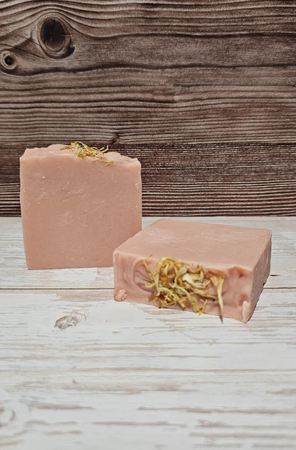 Two pink soap bars with greenery on a wooden surface