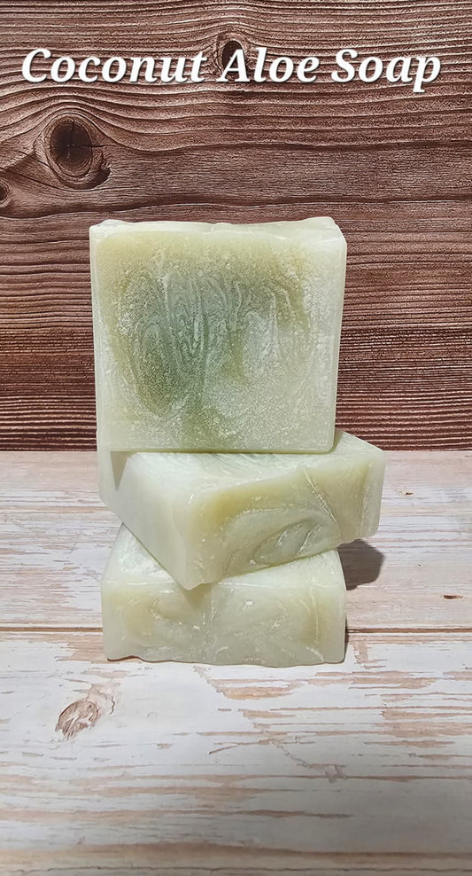 Three bars of coconut aloe soap stacked on a wooden surface with 'Coconut Aloe Soap' text above.