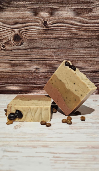 Two layered coffee soap bars on a wooden surface with coffee beans.
