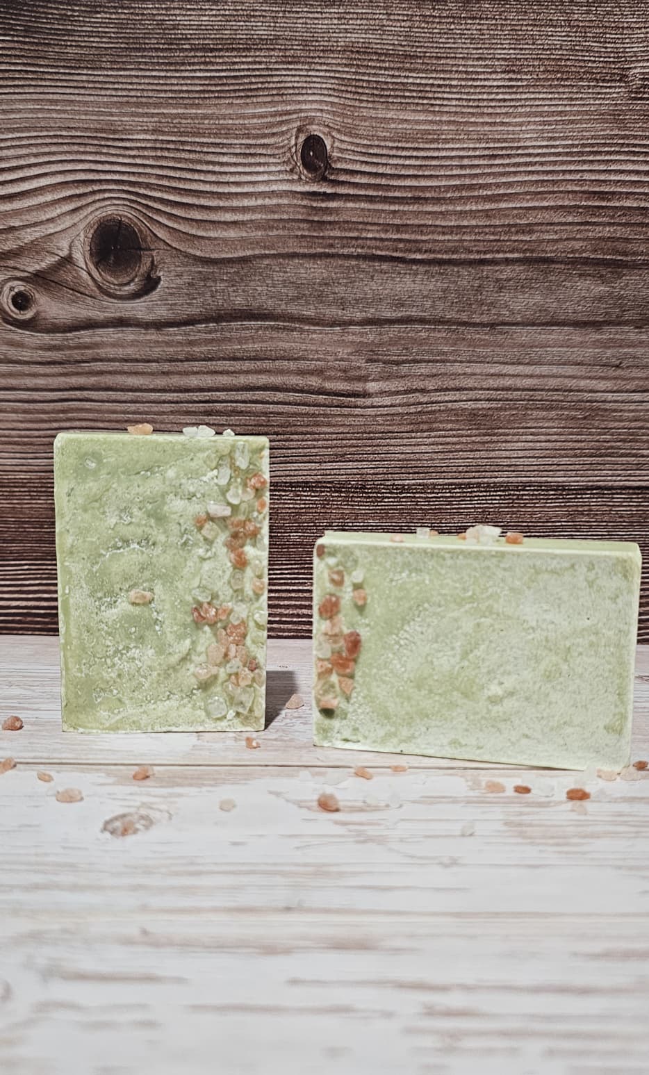 Two green soap bars on a wooden surface with a rustic background