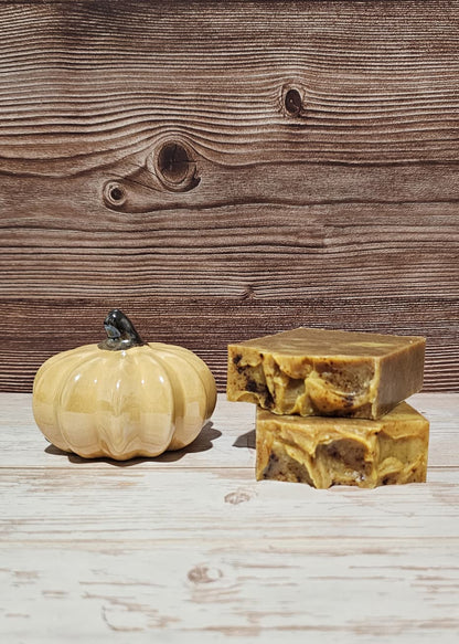 Two bars of soap and a small pumpkin on a wooden surface with a wooden background