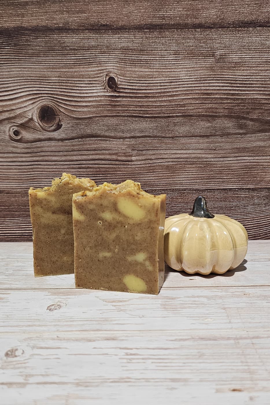 Two bars of soap with a small pumpkin on a wooden surface and background