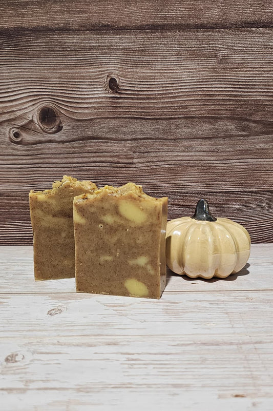 Two bars of soap with a small pumpkin on a wooden surface and background