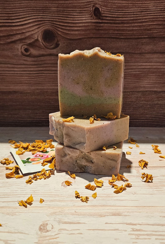 Stack of three handmade soap bars with natural ingredients on a wooden surface.