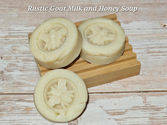 Three rustic goat milk and honey soaps on a wooden block with a light wood background.