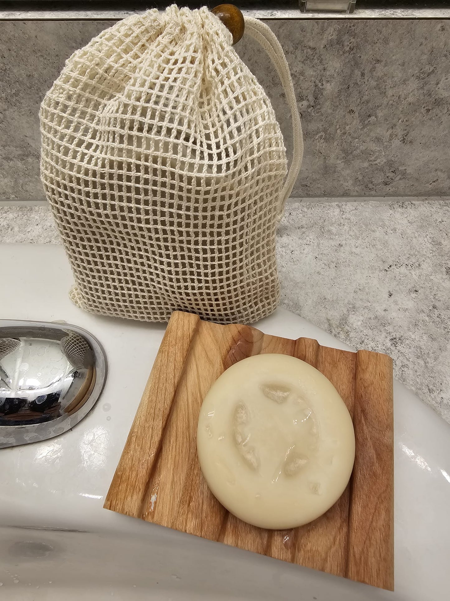 Bar of soap on a wooden soap dish with a mesh bag in the background.