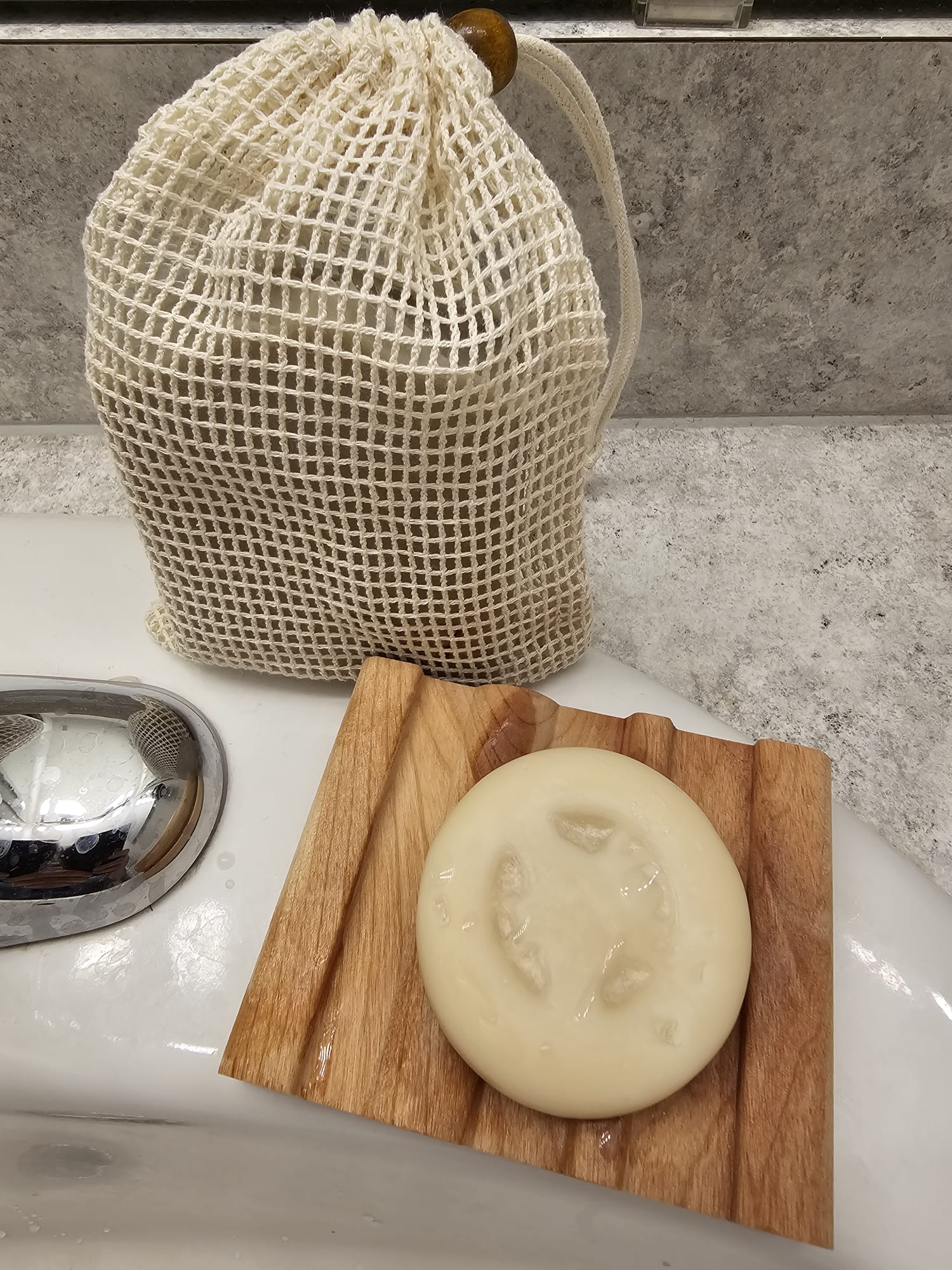 Bar of soap on a wooden soap dish with a mesh bag in the background.