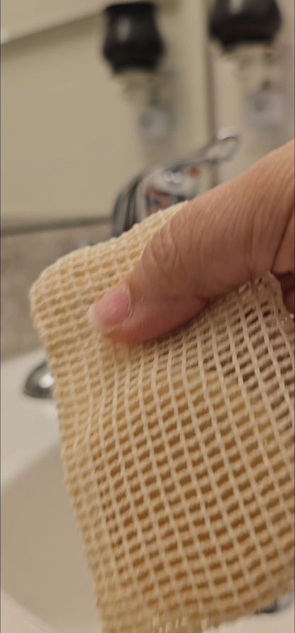 Hand holding a textured beige sponge in a bathroom setting