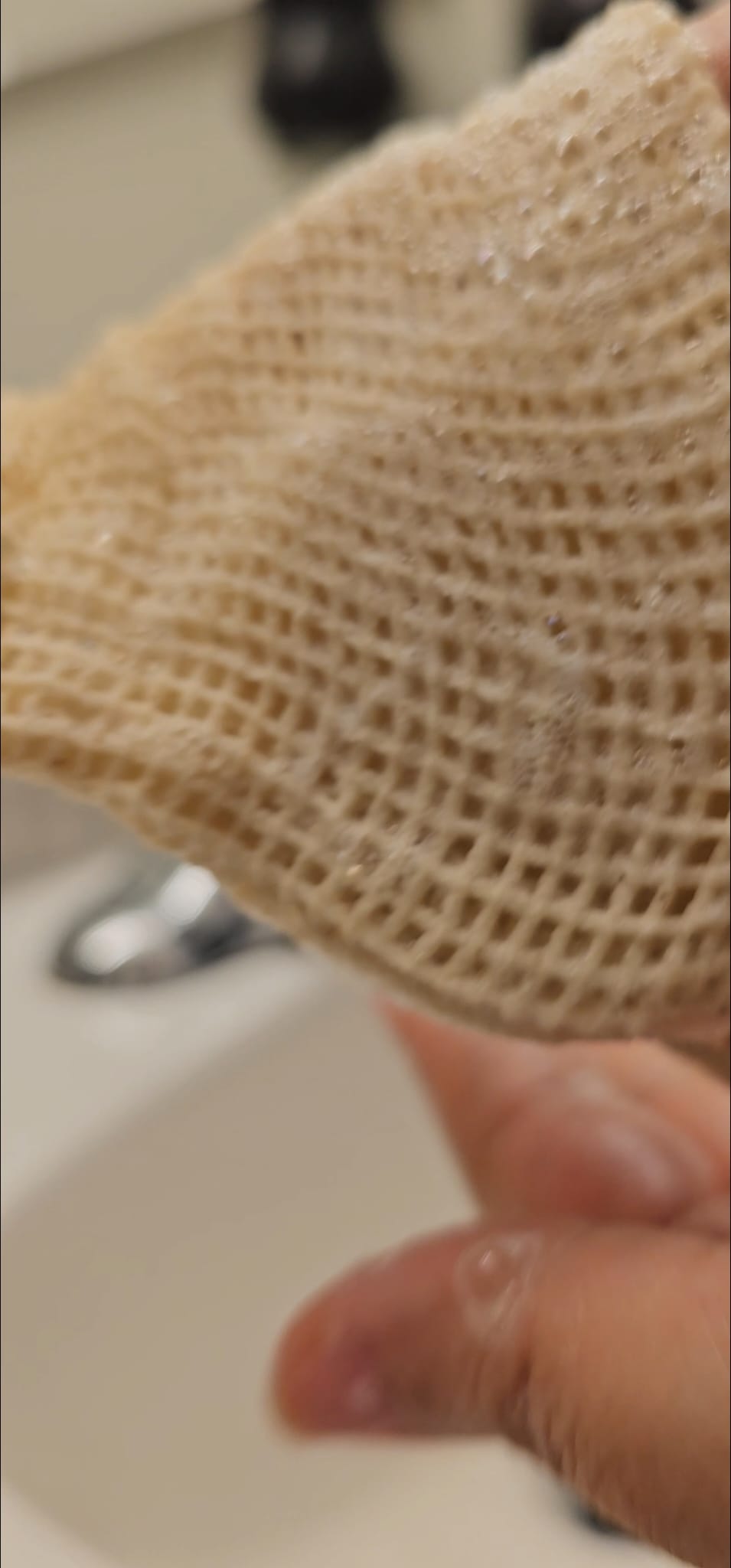 Close-up of a textured beige mesh bag held by a hand with a blurred background.