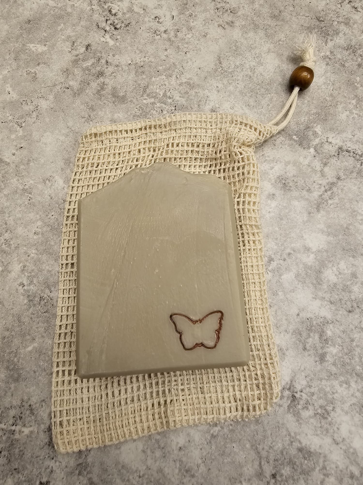 Rectangular soap bar with a butterfly design on a mesh bag against a textured gray background