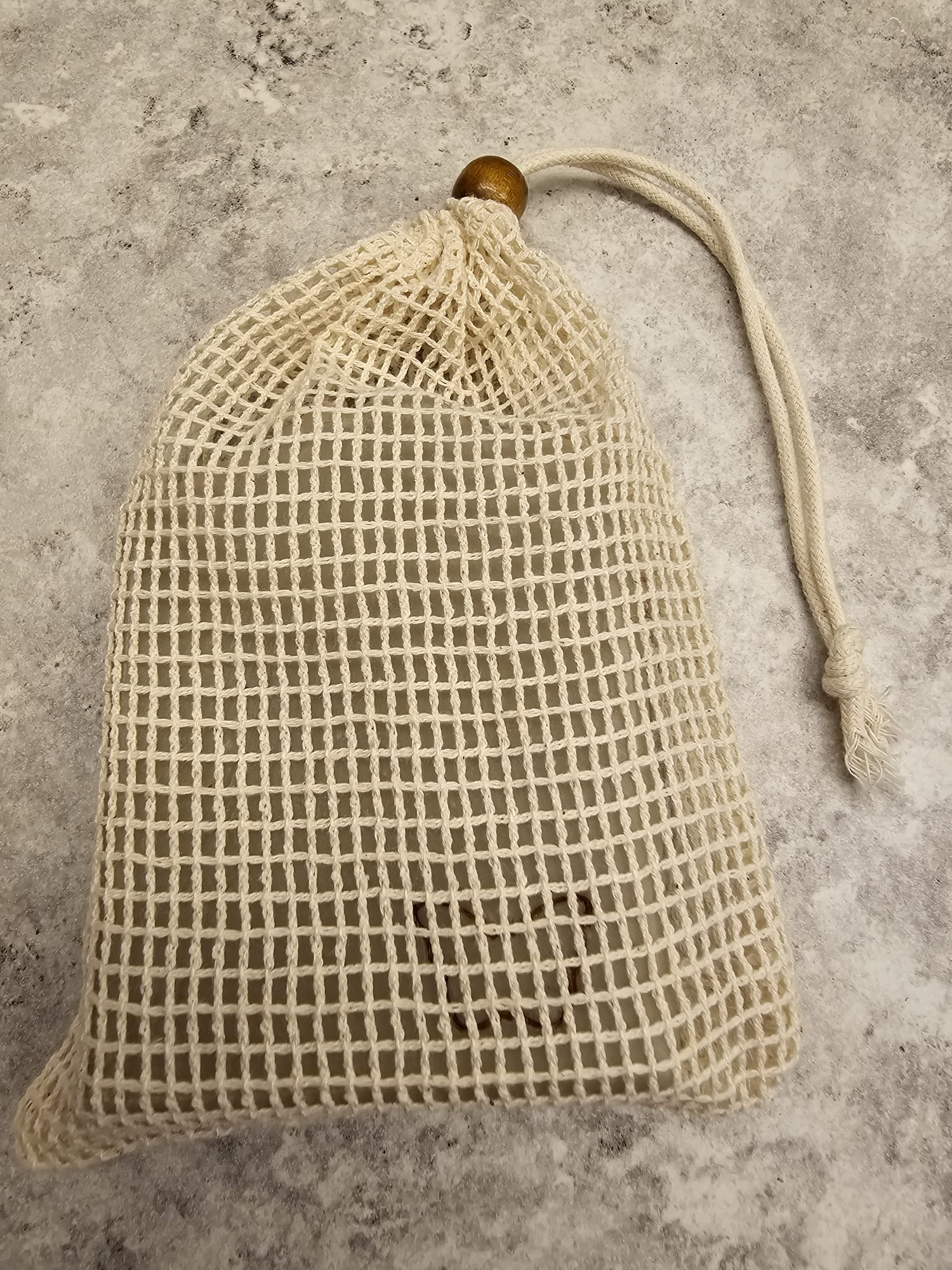 Textured beige soap bag with wooden bead on a gray surface