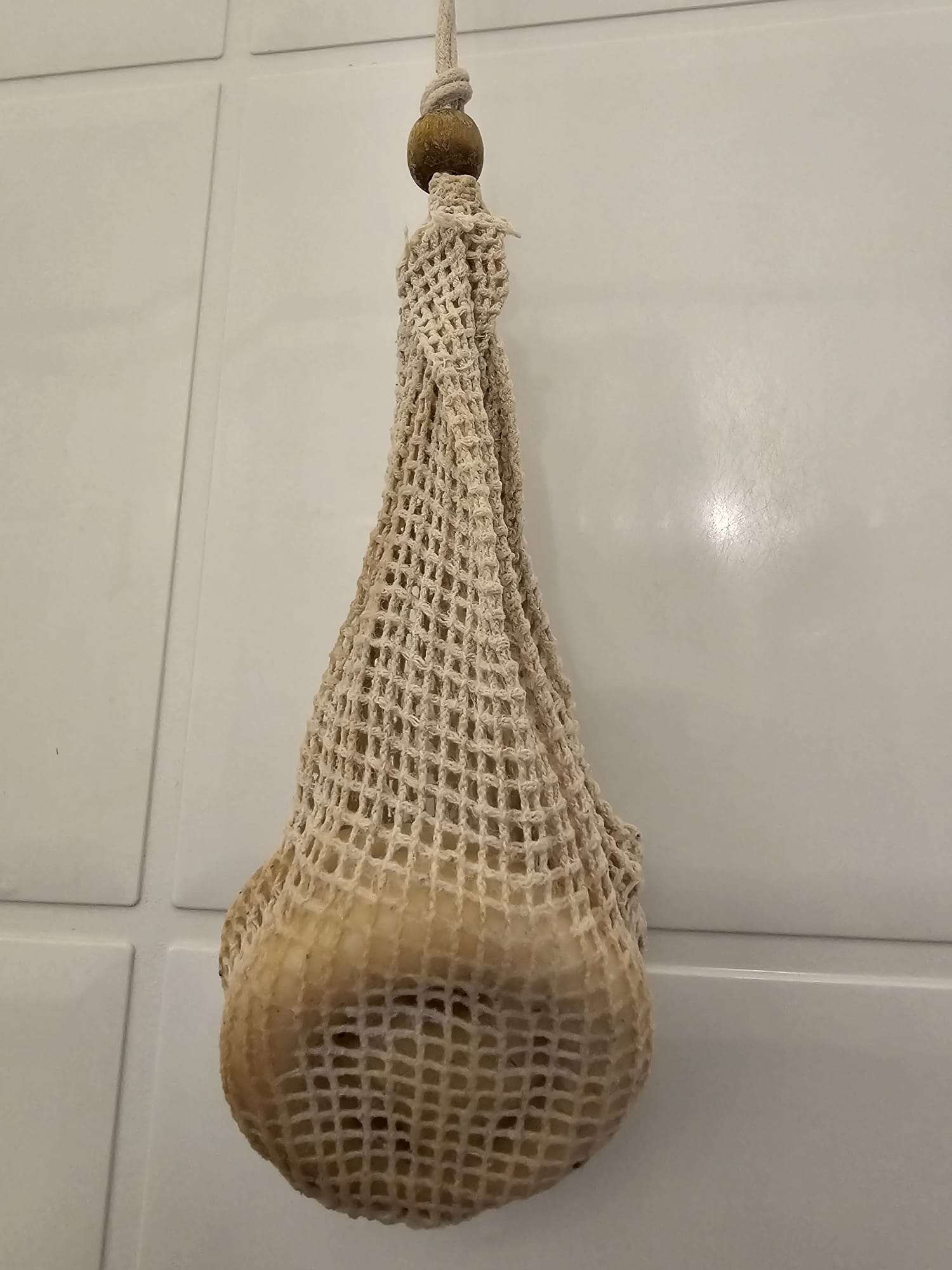 Textured beige bag with a wooden handle hanging against a tiled wall.