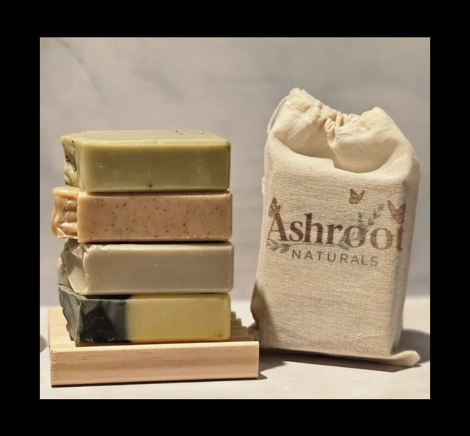 Stack of soap bars on a wooden stand with a plant and a bag labeled 'Ashroot Naturals' in the background.