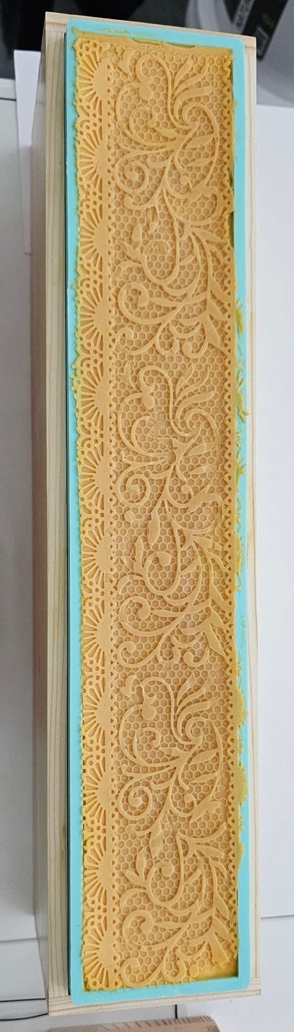 A rectangular piece of textured yellow lace or embroidered fabric with an ornate floral pattern, bordered by a light blue inner edge and a beige outer frame, shown against a white background.