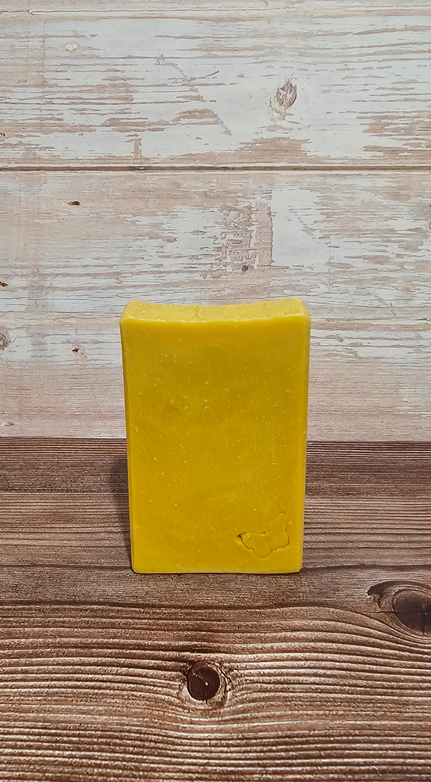 A rectangular bar of yellow soap standing upright on a rustic wooden surface against a whitewashed wood plank background.