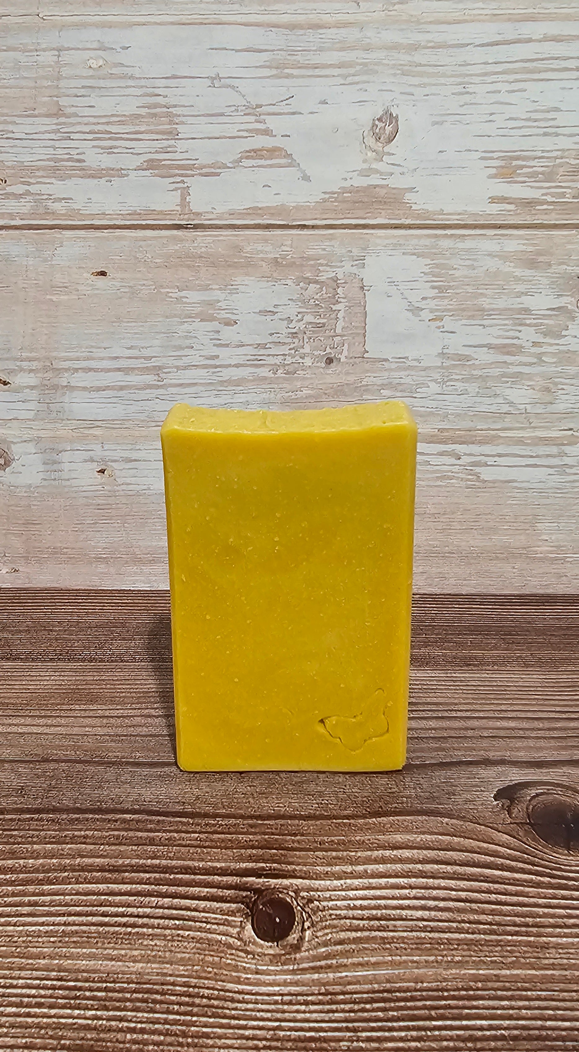 A rectangular bar of yellow soap standing upright on a rustic wooden surface against a whitewashed wood plank background.