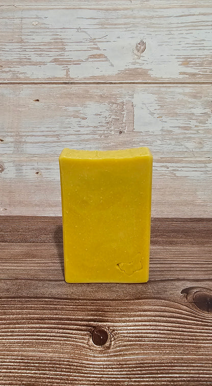 A rectangular bar of yellow soap standing upright on a rustic wooden surface against a whitewashed wood plank background.