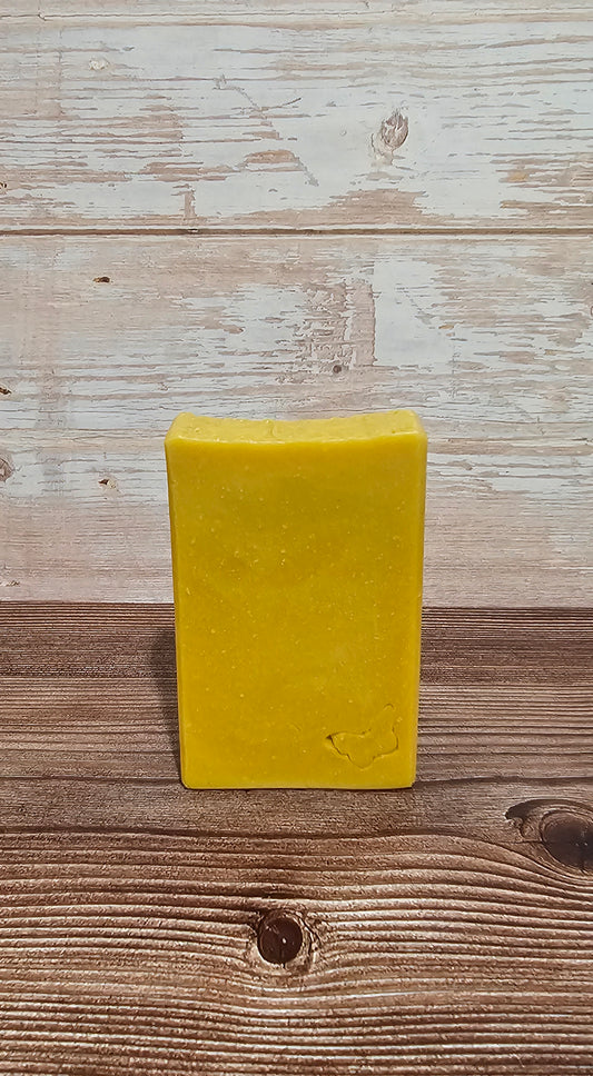 A rectangular bar of yellow soap standing upright on a rustic wooden surface against a whitewashed wood plank background.