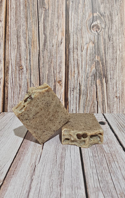 Two rectangular bars of speckled stone-like soap standing on a rustic whitewashed wooden surface, with a matching wood plank backdrop.